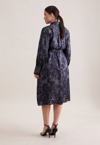 Abito a maniche lunghe in satin grigio scuro con motivo a stampa leopardata. Presenta una vita con cintura e un orlo a ginocchio.