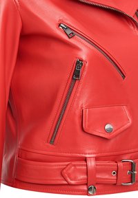 Rode leren motorjack met zilveren ritsen, een riem met gesp en meerdere ritszakken. Soepele textuur met gestructureerd ontwerp.