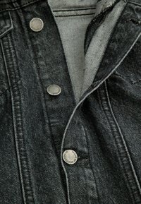 Czarna dżinsowa kurtka z srebrnymi detalami. Posiada klasyczne napy, wyraźny kołnierz i miękkie szare podszycie. Widoczne szczegóły fakturowanego materiału.