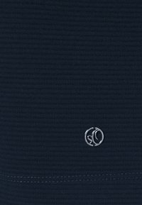 Tessuto blu navy con texture a righe, caratterizzato da un piccolo logo argentato al centro in basso e un dettagliato punto di cucitura discreto.