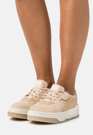 Zapatillas de ante beige con una gruesa suela blanca, que cuentan con cordones redondos y un pequeño logo en la lengüeta. Material texturizado y diseño moderno.