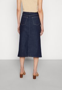 Mörkblå denim midi kjol med rak skärning, två bakfickor och kontrasterande sömmar, bäres med bruna blockklackade sandaler.