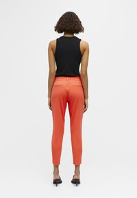 Zwarte mouwloze top met een ronde halslijn, gecombineerd met koraalkleurige slim-fit broek met een elastische tailleband en achterzakken.