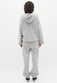Grå, huva sweatshirt och matchande sweatpants av mjukt material. Outleten har elastiska ärmslut och en avslappnad passform, ihop med svarta sneakers.