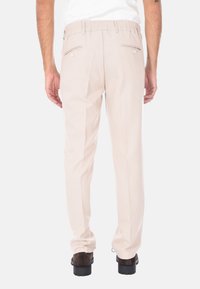 Pantaloni beige con una superficie liscia, dotati di una vita elastica, due tasche posteriori con chiusura a bottone e dettagli a pieghe.