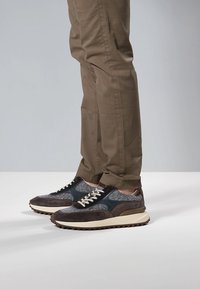 Heren sneakers met een combinatie van donkerbruine suède en grijs stof. Voorzien van een witte rubberen zool, metalen oogjes en grijze veters.