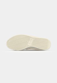 Shoe sole with textured rubber, featuring a zigzag pattern and logo. The design has a light beige color with gray and peach accents.