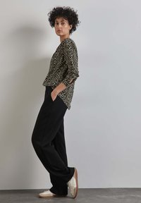 Schwarz und weiß gestreiftes Langarmshirt, lockere Passform, kombiniert mit schwarzen weiten Hosen und weißen Sneakers, die einen lässigen Look präsentieren.