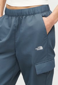 Άτομο που φοράει μπλε παντελόνι με ελαστική μέση και τσέπη cargo, με το λογότυπο The North Face στο δεξί μηρό, το χέρι ακουμπισμένο στην πλαϊνή τσέπη.