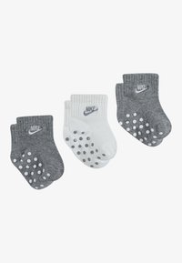 Tres pares de calcetines: uno blanco con logo gris, dos grises con puntos blancos, todos hechos de tejido suave, con puños acanalados y marca Nike.