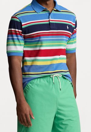 Polo w paski w wielu kolorach z niebieską kołnierzykiem i krótkimi rękawami, zestawiony z zielonymi szortami. Posiada małe logo na klatce piersiowej.