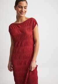 Red, textured dress with a boat neckline and short sleeves, featuring pleated details and a fitted shape that flows to the knee.