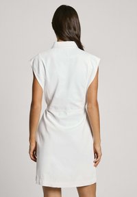 Witte, korte mouwen jurk met een kraag en riem. Glad materiaal met een strakke silhouet en een lengte boven de knie.