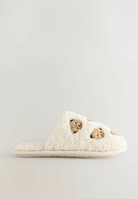 White fuzzy slipper with a textured surface, featuring tan circular accents. The design has a slip-on shape and a flat sole.