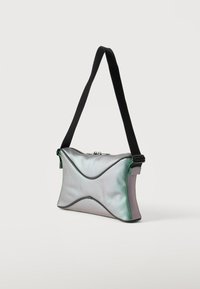 Μικρό ασημί τσαντάκι με μαύρο ρυθμιζόμενο λουρί ώμου και καμπυλωτές λεπτομέρειες ραφής, απεικονισμένο σε απλό φωτεινό φόντο.