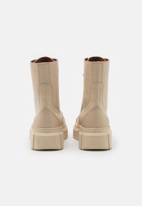 Botas de tornozelo em pele bege com sola robusta, apresentando detalhes de costura e uma textura suave, desenhadas para um look contemporâneo.
