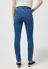 Vaqueros de denim azul con una cintura alta, ajuste slim y costuras en contraste, que presentan patrones zigzagueantes distintivos en los bolsillos traseros.
