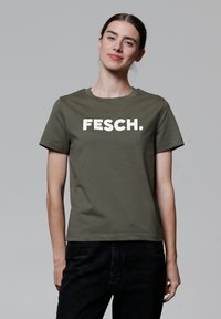 Olivgrünes T-Shirt mit kurzen Ärmeln aus Baumwolle, das auf der Vorderseite einen weißen Blockdruck mit "FESCH." und einen runden Halsausschnitt hat.