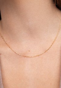Collier en chaîne dorée avec des maillons ovales allongés, texture lisse, reposant légèrement sur la clavicule. Design simple, sans accents supplémentaires.