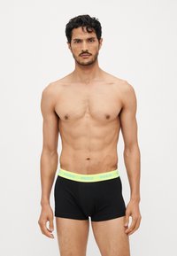 Schwarze Boxershorts mit einem neongelben Gummibund, der das Logo "HUGO" zeigt. Der Stoff wirkt glatt und enganliegend und präsentiert ein modernes Design.