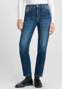 Jean en denim bleu foncé avec une coupe droite, présentant une taille haute, cinq poches et une finition légèrement délavée. Accentué par des coutures dorées.