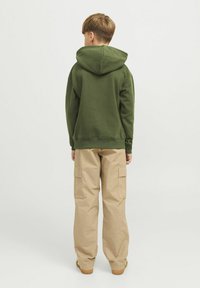 Sudadera verde con capucha y corte holgado, combinada con pantalones cargo de color beige claro que cuentan con bolsillos laterales. Se ve casual y cómoda.