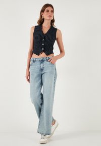 Námornícky pruhovaná krátka vesta s gombíkmi skombinovaná s svetlomodrými širokými džínami a bielymi teniskami. Hladký materiál a voľný strih.