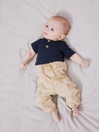 Marineblauw geribd T-shirt met korte mouwen en twee knopen aan de voorkant; beige cargo pants met elastische boorden en zakken; liggend op een lichtgekleurde vlakke ondergrond.