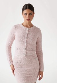 Pink tweed cardigan with long sleeves, round neckline, and decorative buttons. Features two pockets with similar button accents.