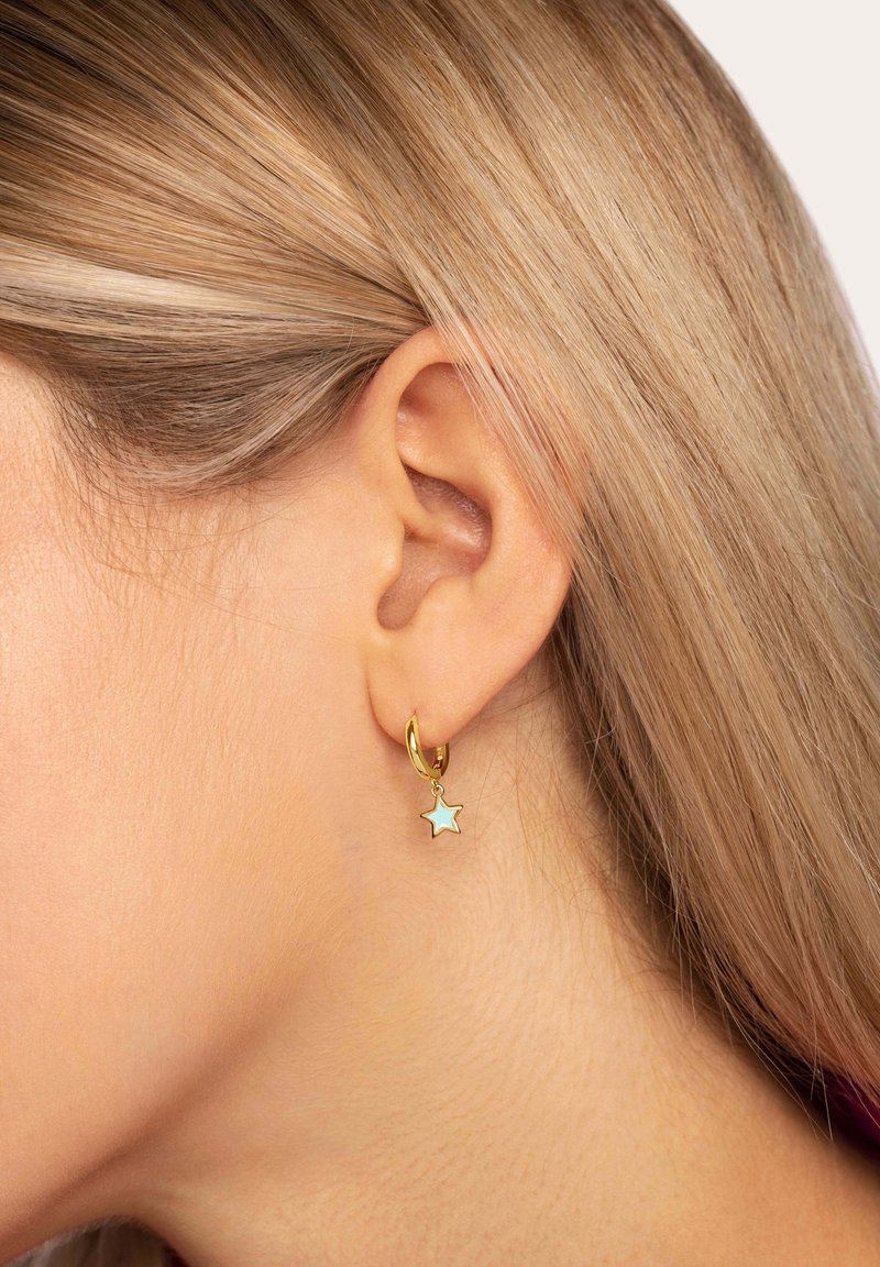 Boucle d'oreille en or ornée d'un petit charm étoile avec un incrustation bleu clair, suspendue à la boucle avec une finition lisse et polie.