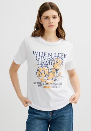 Joven mujer con camiseta blanca con gráficos de limones y vaso y texto: «Cuando la vida nos da limones, hacemos una limonada increíble y un meme sobre ello.»