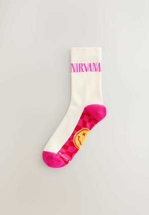 Biała skarpetka crew z różowym logo "NIRVANA", ozdobiona grafiką uśmiechniętej twarzy oraz wzorem w szachownicę w odcieniach różu i żółci na stopie.