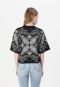 Svart topp med hvit paisley-print, korte ermer, rund hals, strukturet stoff og avslappet passform. Bæres med lyseblå jeans.