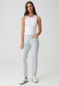 Pantalons en coton bleu clair avec une taille à cordon de serrage, des poches avant et une coupe slim. Associés à un débardeur blanc et des baskets blanches.