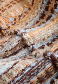 Tissu en laine présentant des motifs complexes en beige, caramel, bleu clair et marron, affichant un aspect texturé et stratifié.