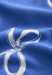 Modrá látka s hladkým povrchem, s opakujícím se vzorem bílých stužek. Design zahrnuje podrobné obrysy stužek a uzlové akcenty.