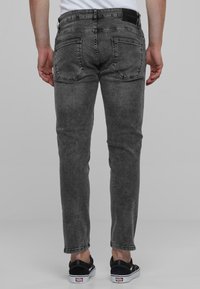 Jeans skinny de mezclilla gris con un acabado desgastado, con bolsillos traseros y una etiqueta de cuero en la cinturilla, combinados con zapatos negros.