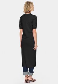 Robe midi noire avec des manches courtes bouffantes, une coupe droite et une texture lisse, associée à un denim roulé et des chaussures à talons bloc à motifs.