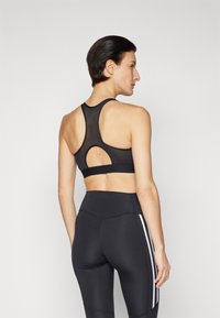 Soutien-gorge de sport noir avec un panneau en mesh et un design dos nageur. Présente un détail découpé et se marie avec un legging noir taille haute avec des rayures blanches.