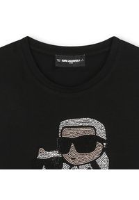 Fekete pamut póló flitteres grafikával, amely napellenzős karaktert ábrázol, kerek nyakkivágással és rövid ujjakkal.