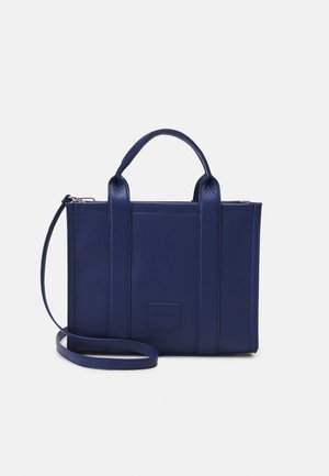 Sac à main rectangulaire en cuir bleu marine avec deux poignées, une bandoulière amovible et une petite étiquette à l'avant.