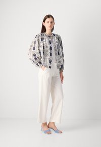 Blusa a maniche puff, a fantasia blu navy e bianca, abbinata a pantaloni palazzo a vita alta crema e sandali con tacco blu chiaro.