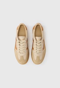 Paar beige und hellbraune Schnürsneaker mit Wildledereinsätzen, von oben auf einem schlichten weißen Hintergrund betrachtet.