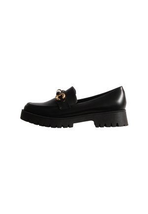 Mocassin noir en cuir avec un ornement doré et une épaisse semelle plateforme rainurée, présenté de profil sur fond blanc.