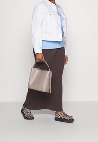 Leichte weiße Jeansjacke, blaues Oberteil, gerippter brauner Rock, graue Tragetasche und schwarze Sandalen mit weißem Blumenmuster.