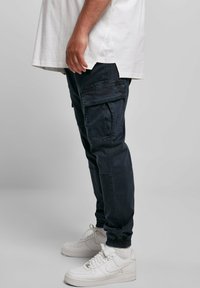 Marinblå cargobyxor med flera fickor, elastiska ankle cuffs och en avslappnad passform, ihop med vita sneakers och en lös vit skjorta.