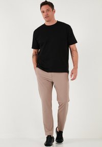 Zwarte katoenen T-shirt gecombineerd met lichtbeige slim-fit broek en zwarte sneakers. Eenvoudig ontwerp, korte mouwen en geen zichtbare patronen.