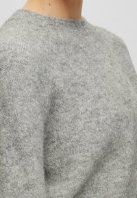 Ljusgrå ulltröja med rund hals, med en mjuk textur och en något marmorerad utseende. Detalj runt halsringningen är synlig.