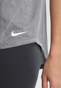 Grå sportskjorte med rundet kant og korte ærmer, prydet med et hvidt Nike-logo på venstre side. Sammenholdt med sorte leggings.