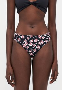 Blomsterbikini-bunn med svart bakgrunn og rosa og hvite blomster. Laget av mykt stoff, har den en lav midje og glatt tekstur.